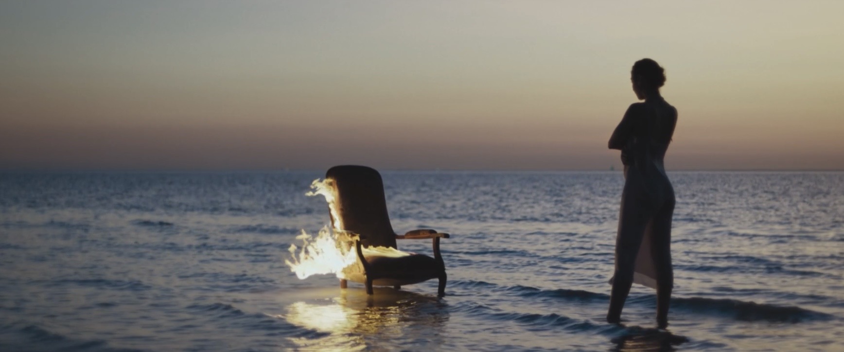 Plan du clip As Animals : fauteuil en feu au bord de la mer au crépuscule